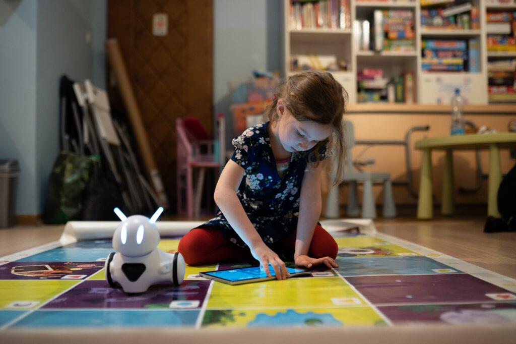 Robotyka Dziewczynka siedzi na podłodze i patrzy na tablet, obok robot